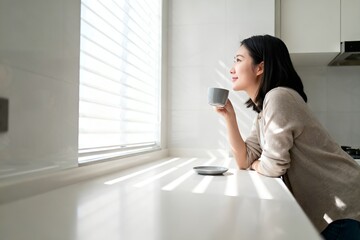 Obraz premium Woman Enjoying Coffee by Kitchen Window Morning Sunbeams