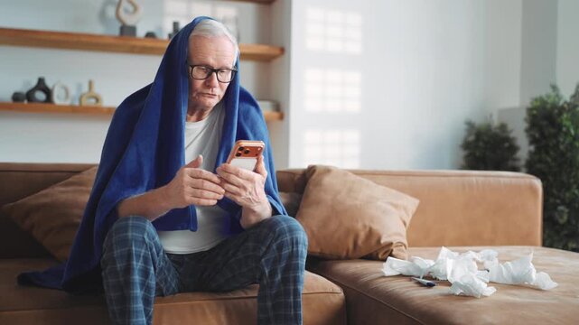 Old man feeling bad when catch cold, surfing internet by smartphone at home. Elderly male person chatting online with friends or wife in mobile app or looking for information of curing influenza