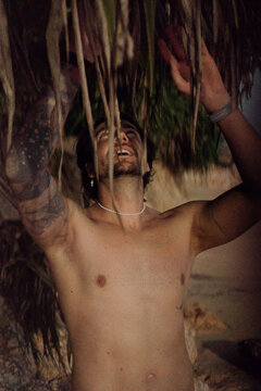 Shirtless tattooed man under pandanus tree, Nyang Nyang Beach