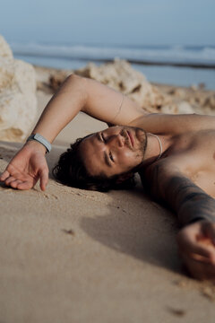 Shirtless man lying on sand eyes closed, Nyang Nyang, Bali