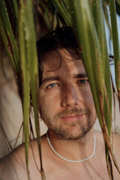 Close up portrait of man with sand on face through pandanus leaves