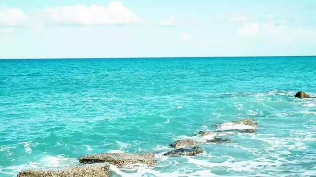 View of the Mediterranean Sea with small waves crashing on the rocks during a sunny day. The video was shot in the seaside village of Rodia, near Messina, Sicily, in Southern Italy