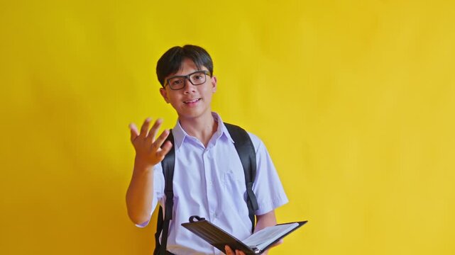 Smart teenage boy in school uniform holding folder and gesturing while talking against yellow background
