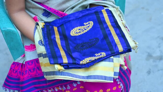 A person holds a blue silk saree with golden motifs showcasing traditional Assamese textile craft in Byaskuchi village, Assam. Highlights cultural fashion.