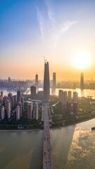 Fototapeta premium An aerial view captures a sprawling cityscape bathed in the warm glow of a setting sun, showcasing modern architecture and a prominent bridge connecting the urban landscape.