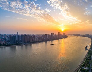 Naklejka premium An aerial view captures a sprawling cityscape along a wide river at sunset, showcasing a blend of modern architecture and natural beauty.