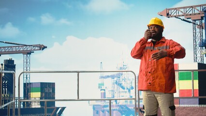 Expert inspects integrity of offshore platform infrastructure, speaking in walkie talkie. African american man on drilling rig using handheld radio device to communicate malfunctions, © DC Studio