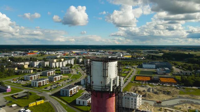 Aerial drone video flying around a tall smoke stack chimney tower that has 5G and 6G electronic transmittors and radio equipment on it during a sunny day in a small city area at summer time.