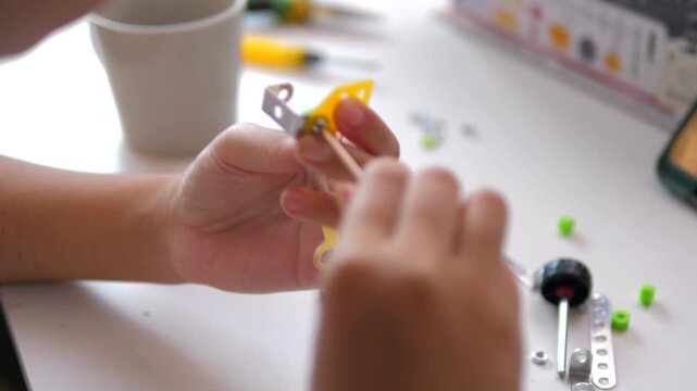 Close up of child hands assembling 3D printed robot model on table. Concept of STEM education, robotics learning, creativity, and technology development