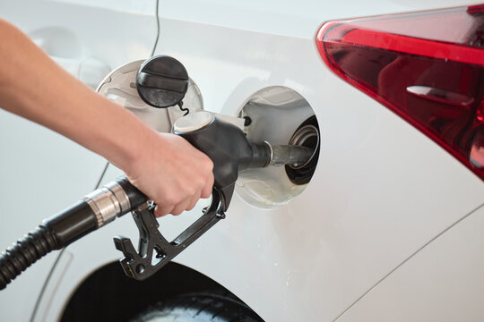 Close up of a person refueling a car with a fuel nozzle at a gas station. Concept of energy, transportation and fuel consumption.