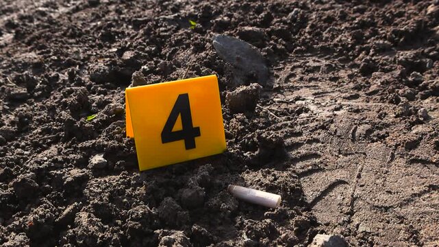 Close up footage of a yellow colored crime scene marker next to a cigarette bud and a footprint left behind by a criminal on a muddy wet countryside road or ground. The marker has number 4 on it, dna.