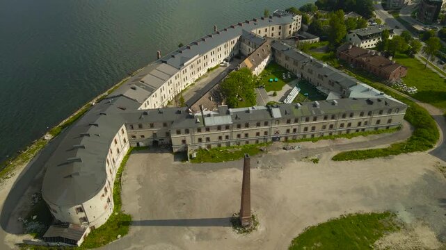 Aerial drone footage flying above a large seaside shoreline Patarei fortress that was once a large prison in Tallinn Estonia northern Baltic shoreline. Blue ocean sea and grassy areas visible in sun.