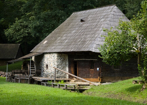 Traditional wooden watermill with an overshot water wheel, stone foundation, and wooden shingle roof at the Astra Museum in Sibiu, Romania.