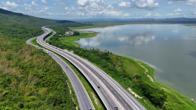 Aerial view of highway running along river and green hills. Transportation, infrastructure, travel and logistics concept