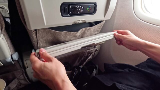 Passenger folding away airplane tray table, preparing for takeoff or landing on commercial flight.