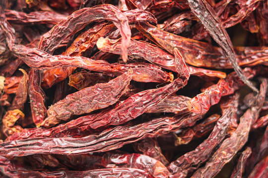 A textured pile of long, wrinkled dried red chili peppers, commonly used as a base for spicy condiments and seasonings.