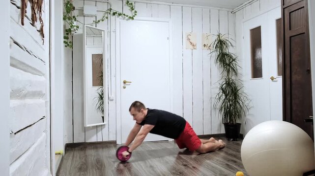 Caucasian man performing an abs wheel rollout exercise at home. Movement emphasizes core strength, stability and endurance, showcasing the concept of functional training and fitness improvement. 4k.