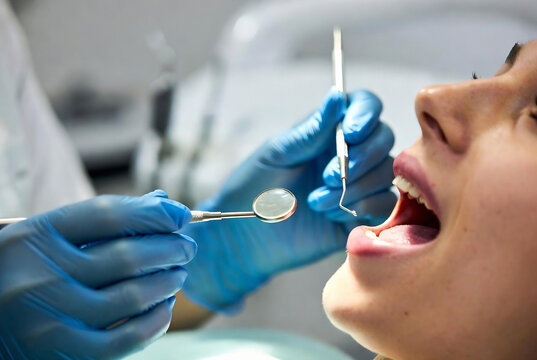A dentist is examining a patient&rsquo;s mouth with a dental mirror and probe. It's taking place in a dental office.