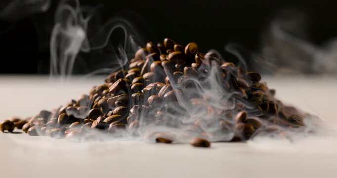 A pile of roasted coffee beans emits gentle steam, creating a rich, aromatic atmosphere against a dark background. Shallow depth of field highlights texture and warmth