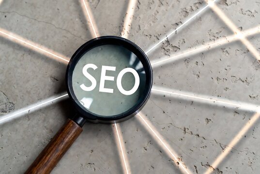 A magnifying glass with "SEO" on it is examining a textured concrete surface.