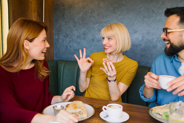 Naklejka premium Happy young adults enjoying meal together while one woman shows approval gesture during casual social gathering