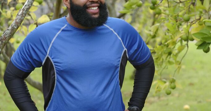 African American man standing near fruit tree while camera pulling back, smiling in blue shirt
