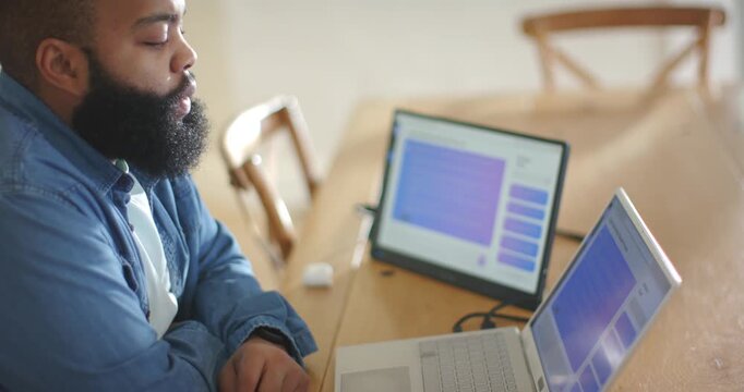 Leaning in, African American man tapping laptop at desk, glancing at tablet, reviewing slide