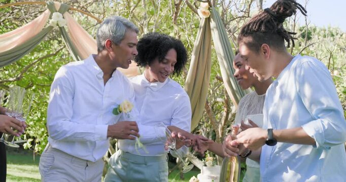Diverse group seeing man opening bottle popping cork pouring flutes under fabric arch toasting ring