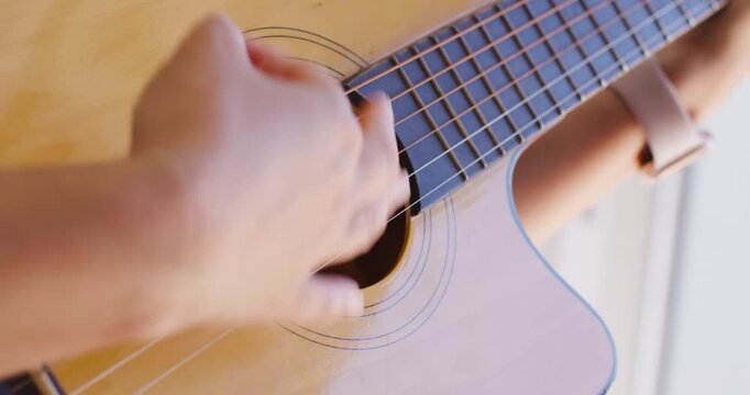 Guitarist hands beside bright window, moving across guitar, plucking and strumming while practicing