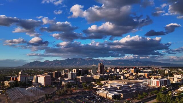 Aerial view of Tucson city buildings under a blue sky with puffy white clouds and distant mountains, Tucson, Arizona, United States.