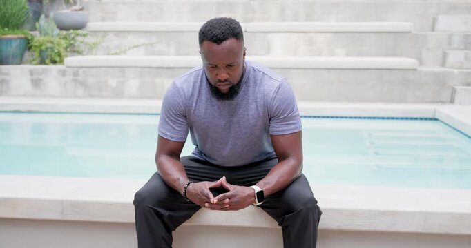 African man sitting on pool coping wearing smartwatch, camera zooming, lifting head meeting lens