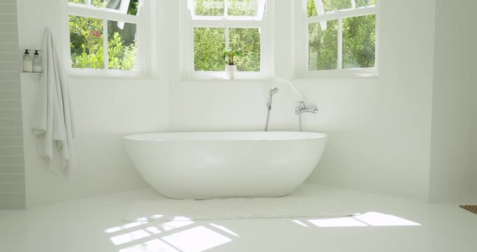 Freestanding oval bathtub sitting centered under three-pane windows catching sunlit floor glow