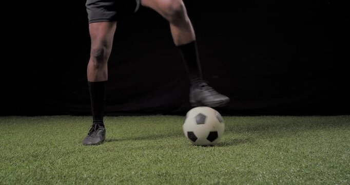 African American male in black cleats practicing ball control on studio turf from stationary ball