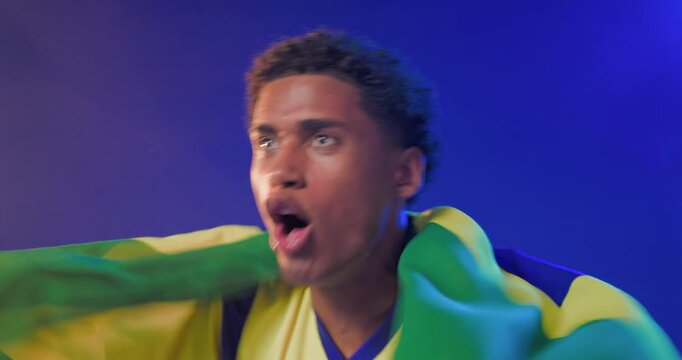 African American man lifting Brazilian flag initiating cheer wearing yellow jersey in studio