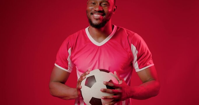 African man reacting to camera cue, cradling soccer ball, smiling then calming for red jersey shoot