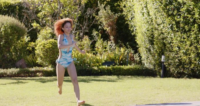 3 female friends in swimwear watching runner running into pool, splashing near pink tube for fun