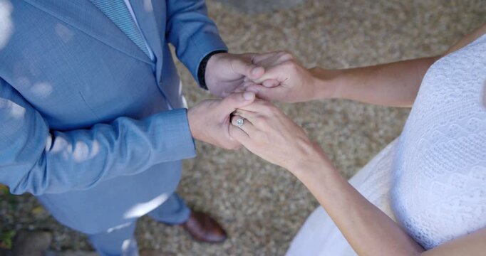 Couple sealing vows under pergola, exchanging rings as bride presenting left hand in white dress