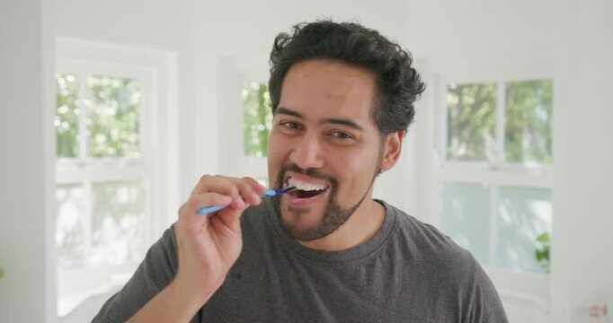 Mid-adult African American man raising blue-handled toothbrush brushing teeth for care in bathroom