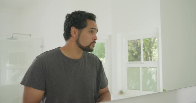 African American man checking product in mirror, rubbing balm into beard at sink shaping neckline