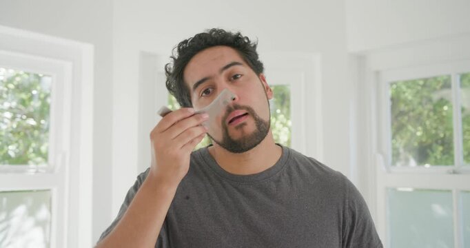 From window light African American man trimming beard using razor, comb at home, checking symmetry