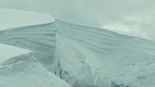 Dramatic close-up of Antarctic glacier edge revealing beautiful layered ice strata and deep crevasse under pale misty sky