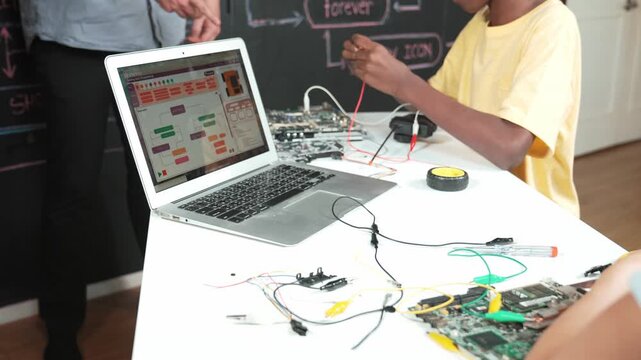 Top view of engineering code or prompt displayed on screen while fixing on mother board. Caucasian teacher teaching about car model construction while teenager study programming system. Edification