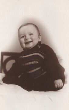 Happy laughing baby sitting upright in striped knit sweater, studio sepia portrait circa 1930s