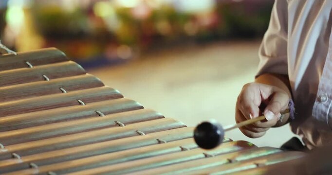 Hands playing a wooden xylophone with mallets, Thai school students perform xylophone outdoors at night market, Showcasing traditional music culture, close-up
