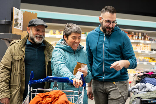 Adult son helping his senior parents during their supermarket shopping, showing care and unity