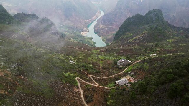 Aerial drone footage of isolated hillside farms above the Nho Que River in a deep misty mountain valley with steep rugged terrain in northern Vietnam.
