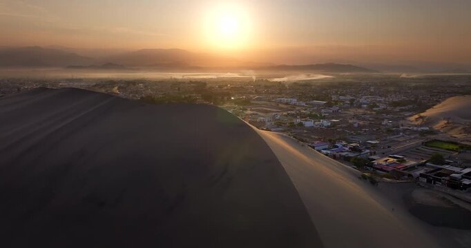 Sun rising over the sand dunes and the desert oasis of Huacachina near the city of Ica, Peru. Aerial forward