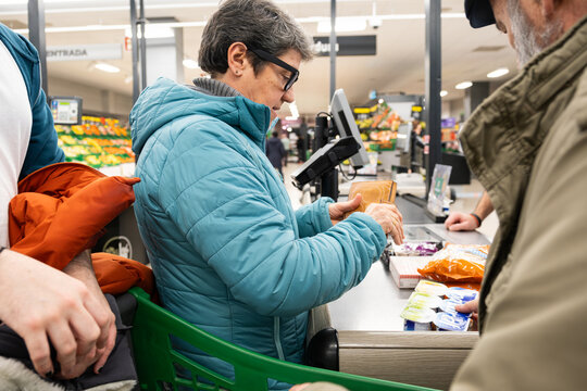 Woman standing at supermarket checkout holding a wallet while paying for groceries
