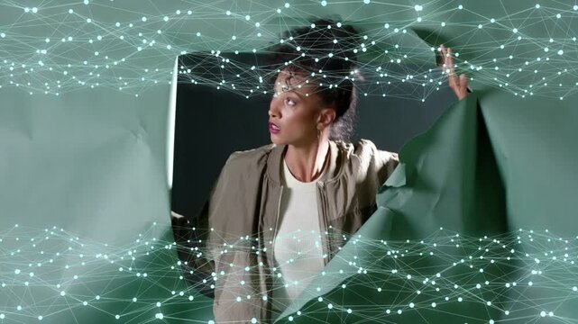 Small rips starting woman tearing open green paper, revealing tech set with node grid intersecting