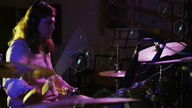 Male drummer playing kit in dim studio, hands hitting causing hexagon syringe overlay, recording